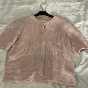 Ljusrosa kofta från Gina Tricot - Superfin ljusrosa kofta från Gina Tricot i ribbstickat material. Koftan har korta ärmar, rund halsringning och knäpps med matchande knappar framtill. Perfekt att slänga över en topp för en söt och chill look. Säljer eftersom den inte kommer till användning.