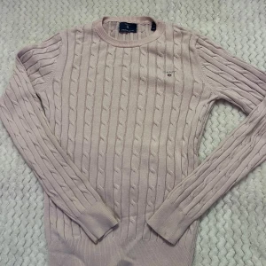 Ljusrosa kabelstickad tröja Gant XS - Supersnygg ljusrosa kabelstickad tröja från Gant i stretchig bomull. Klassisk rund halsringning, passar även en XXS, långärmad och med diskret logga på bröstet. Perfekt för dig som gillar en stilren och fräsch look.