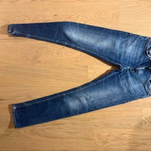  Nudie Jeans, indigo myth,grim tim  - Säljer ett par klassiska blå jeans från Nudie Jeans med snygga slitningar och kontrastsömmar. Jeansen har raka ben, fem fickor och Nudie-logga på bakfickan. Tillverkade i mjuk bomullsdenim med en skön passform. Färg indigo myth. Modell grim tim.