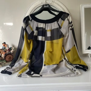 Mönstrad blus från Soyaconcept - Säljer en luftig blus från Soyaconcept med grafiskt rutigt mönster i svart, vit, gul och grå. Blusen har långärmade transparenta ärmar med knäppning vid mudden och rundad halsringning. Materialet är lätt och skönt polyester, perfekt för dig som gillar färg och mönster.