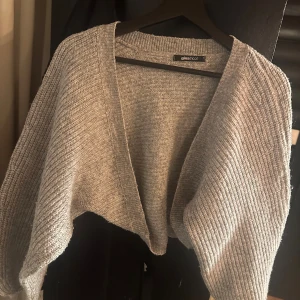 Grå croppad kofta från Gina Tricot - Supermjuk och stickad grå kofta från Gina Tricot. Modellen är croppad med lång ärm och öppen framtill, perfekt att slänga över en topp. Ribbstickad struktur som ger en chill och trendig vibe. Storlek S, knappt använd så i väldigt bra skick.