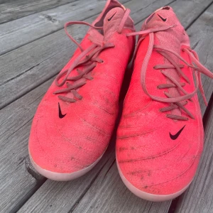 Nike Flyknit fotbollsskor rosa - Säljer ett par Nike Flyknit fotbollsskor i en riktigt snygg rosa färg med svarta detaljer och snörning. Skorna har rund tå, platt sula med dobbar och är tillverkade i lätt och smidigt syntetmaterial för bästa känsla på planen.