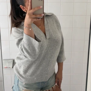 Grå stickad tröja - Supermjuk grå stickad tröja från H&M med snygg krage och v-ringning. Tröjan har trekvartsärmar och ribbade muddar nertill. Perfekt för lager-på-lager och chill vibes. Denna tröja är i ett fint skick, och säljer då jag inte använder den längre. Vid frågor hör av er💕