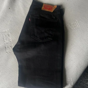 Svarta Levi's 501 jeans W33 L32 - Svarta klassiska Levi's 501 jeans med rak passform och femficksdesign. Jeansen har den ikoniska läderpatchen bak i midjan och är tillverkade i slitstarkt jeanstyg. Perfekta för dig som gillar tidlös stil och vill ha ett par jeans som funkar till allt.