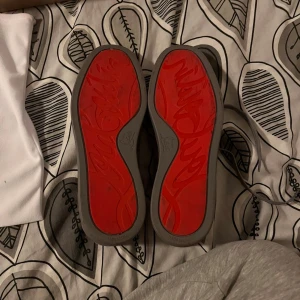 Christian Louboutin grå mockasneakers - Säljer ett par exklusiva sneakers från Christian Louboutin i grå mocka med ikonisk röd sula. Skorna har snörning, rund tå och platt sula. Kommer med originalpåse, box och kvitton. Perfekta för dig som vill sticka ut med lyxig streetstyle.