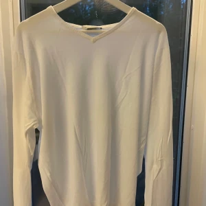 Vit bomullströja John Smedley L - Vit långärmad tröja från John Smedley i exklusiv Sea Island-bomull. Tröjan har en klassisk v-ringning och är tunnstickad med en clean och stilren look. Perfekt för dig som gillar minimalistisk stil och premiumkänsla.