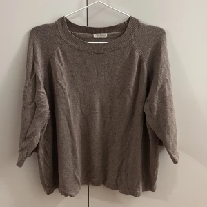 Brun stickad tröja Movesgood - En enkel och stilren brun stickad tröja från Movesgood. Tröjan har rund halsringning och långa ärmar, perfekt för lager på lager under kyliga dagar. Mjuk och skön känsla som passar till jeans eller kjol. Liten i storleken