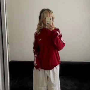 Röd träningsjacka från Adidas - Snygg röd träningsjacka från Adidas med de klassiska tre vita ränderna längs ärmarna. Jackan har dragkedja och Adidas-logga på bröstet. Köpt här på plick men är i bra skick!