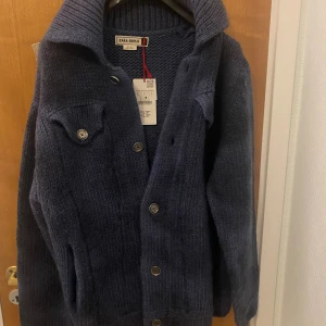 Mörkblå stickad cardigan jacka Zara SPRLS - Säljer en mörkblå stickad cardigan jacka från Zara SRPLS. Jackan har grovstickad struktur, stora knappar framtill och en bred krage. Perfekt för lager-på-lager och chill stil. Fickor med knappdetaljer på bröstet och långa ärmar.