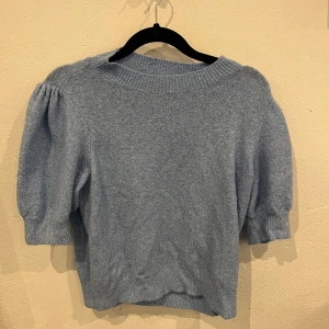 Ljusblå stickad tröja med puffärm -  ljusblå stickad tröja med korta puffärmar och trekvart armar, bred ribbad kant vid halsen. Materialet är mjukt och känns riktigt skönt mot huden.