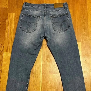 Tiger of Sweden Jeans - Säljer ett par ljusblå Tiger of Sweden Pistolero jeans i storlek 30x32. Slim fit-modell i exklusivt Candiani-denim från Milano, Italien (sedan 1938). Jeansen är i bra skick förutom två mindre lagningar på bakfickorna där tyget lossnat lite, vilket skapat små nästan osynliga hål – därav priset.
