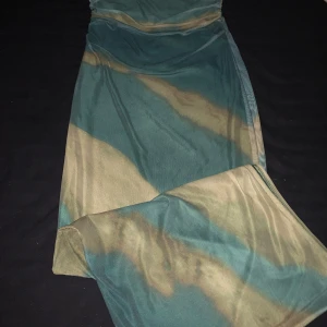 Grön och beige långklänning - Snygg långklänning i mesh med unikt mönster i grönt och beige. Klänningen har en kroppsnära passform och är tillverkad i ett tunt, stretchigt material som ger en cool och trendig look.