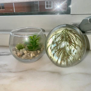 Dekorativ inredning - Bilderna visar en dekorativ glasvas med konstgjorda växter och stenar samt en glaskula med guldfärgade detaljer från Søstrene Grene. Båda produkterna är i bra skick utan synliga skador eller slitage, men har använts länge.