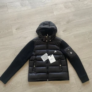 Svart moncler cardigan - Jag säljer den eftersom att den är för liten på mig och är knappt använd. Den är perfekt för den svenska hösten och vintern. Glansen är matt inte väldigt glansig. Den passar från 175-180. Skriv gärna till mig om du har några fler funderingar