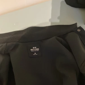 Svart overshirt från Only & Sons - Svart overshirt från Only & Sons i storlek M. Snygg klassisk design med krage, bröstfickor med lock och knappar framtill. Materialet är ullblandning som ger en skön och lite ruggad känsla. Perfekt att ha som lager över en t-shirt eller hoodie.