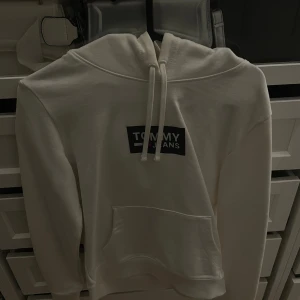 Vit hoodie från Tommy Jeans XS - Säljer en stilren vit hoodie från Tommy Jeans i storlek XS. Tröjan har klassisk huva med snörning, magficka och tryckt logga framtill. Perfekt för en chill och avslappnad look. Materialet är mjukt och skönt, troligtvis bomullsmix.