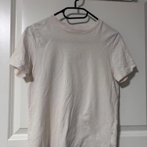 Vit basic t-shirt från H&M - Enkel och stilren vit t-shirt från H&M i mjuk bomull. Klassisk rund halsringning och korta ärmar. Perfekt till jeans eller shorts för en clean look.
