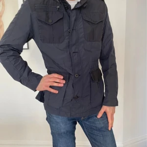 Mörkblå vindjacka från Fortezza - Snygg mörkblå vindjacka från Fortezza med flera praktiska fickor och knappar framtill. Jackan har hög krage, lång ärm och detaljer i svart på bröst- och sidfickor. Perfekt för dig som vill ha en stilren och funktionell jacka. Väldigt snygg höstjacka det står att det är 52 men jag skulle säga det passar en