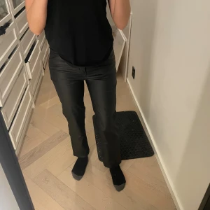 Svarta byxor från Happy Holly - Säljer ett par svarta matta skinnbyxor från Happy Holly med raka ben och normal passform. Byxorna har hög midja och är  Perfekta att styla med en enkel topp eller stickad tröja.