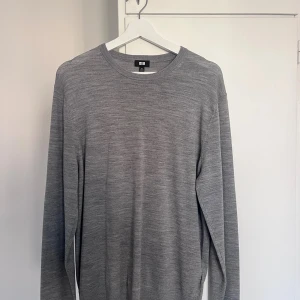 Grå stickad tröja från Uniqlo - En stilren grå stickad tröja från Uniqlo i storlek M. Tröjan har rund halsringning, lång ärm och är tillverkad i ett mjukt material som passar perfekt till lager-på-lager. Enkel och clean look som funkar till allt.
