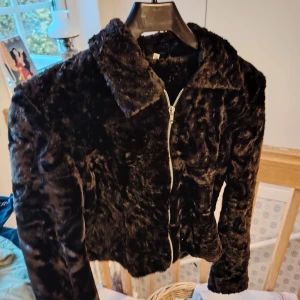 Fuskpälsjacka med dragkedja -- helt ny - Mysig svart pälsjacka med mjuk fuskpäls och klassisk krage. Jackan har hel dragkedja framtill och långärmade ärmar. Perfekt för dig som vill ha en varm och snygg look under kyliga dagar.