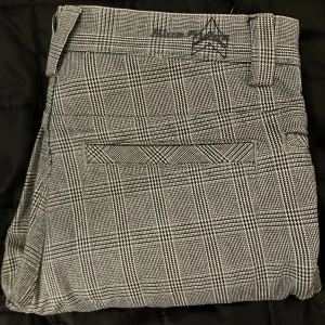 Rutig kostymbyxa från Blue Ridge - Snygga kostymbyxor från Blue Ridge i svartvitt rutigt mönster. Byxorna har raka ben, bälteshällor och är tillverkade i 100% bomull för en skön känsla. Perfekt för dig som gillar klassisk stil med modern twist.