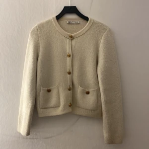 Beige stickad kofta från Zara - den passar mig som brukar ha XS/S.  Superfin beige stickad kofta från Zara med rund halsringning, snygga guldknappar och två fickor framtill. Perfekt att slänga över en t-shirt eller klänning för en chill och stilren look.