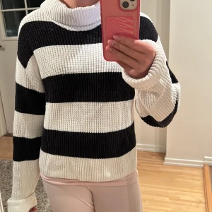 Randig polotröja från Lindex - Säljer en stickad polotröja med breda svarta och vita ränder. Tröjan har en hög krage och långa ärmar. Passar dig som gillar en stilren men ändå cool look.