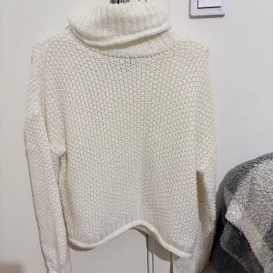 Vit stickad polotröja - Mysig vit stickad polotröja med grovstickad struktur och hög, ribbad polokrage. Perfekt för kyliga dagar och enkel att styla med jeans eller kjol. Storlek S