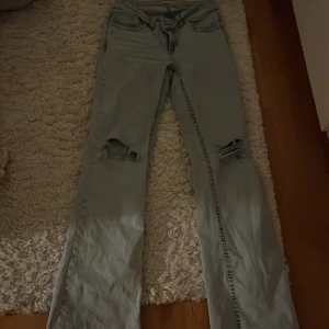 Ljusblå bootcut jeans från Nelly - Säljer ett par ljusblå jeans från Nelly med bootcut passform och slitna detaljer på båda benen. Jeansen har klassiska fem fickor och en snygg broderad bakficka med orange söm. Perfekta för en trendig och avslappnad look.