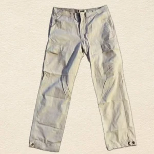 Beige cargobyxor från Tommy Hilfiger - Snygga beige cargobyxor från Tommy Hilfiger med raka ben och flera praktiska fickor på sidorna. Byxorna har klassisk passform, knappstängning och små logodetaljer. Perfekta för en avslappnad streetwear-look.