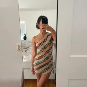 Enärmad klänning - En-ärmad mini klänning i tunt virkat mjukt material med snygga olika färger. Den är i stretch och aldrig använd. Helt ny.