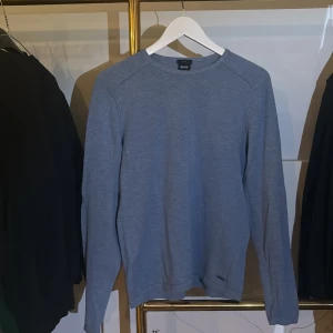 Blå långärmad tröja från BOSS - Snygg blå långärmad tröja från BOSS i slim fit-modell. Tillverkad i 100% bomull för en skön och lätt känsla. Perfekt för dig som gillar stilrena och enkla plagg med en modern passform.