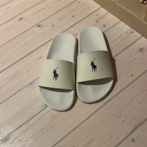 Vita slipers  från Ralph Lauren - Snygga vita sandaler från Polo Ralph Lauren med klassisk logga på ovansidan och Polo-märke under sulan.
