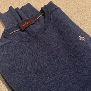 Blå merinoullströja från Morris XS - Snygg blå stickad tröja från Morris i 100% merinoull. Klassisk rund halsringning, långärmad modell och diskret broderad logga på bröstet. Perfekt för dig som gillar stilrena och bekväma plagg med en clean vibe. Tröjan är i xs och är inte använd många gånger 