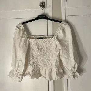 Vit blus Zara - Supersöt vit blus från Zara med puffiga långärmar och smockad kropp. Blusen har volangkant nedtill och elastisk halsringning som kan bäras offshoulder. Perfekt för dig som gillar romantisk och trendig stil.