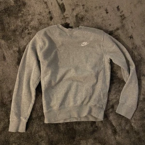 Grå hoodie från Nike - Snygg grå crewneck från Nike med klassisk logga broderad på bröstet. Tröjan har rund halsringning och långa ärmar, perfekt för en chill och sportig stil. Tillverkad i mjuk bomullsblandning som är skön att ha på sig hela dagen.