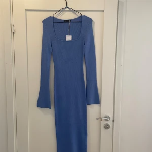 Blå ribbad långklänning Gina Tricot - Säljer en blå ribbad långklänning från Gina Tricot med fyrkantig ringning och långa ärmar med utsvängda ärmslut. Klänningen är figurnära och har en mjuk, stickad känsla. Perfekt för dig som gillar stilrena och trendiga plagg.