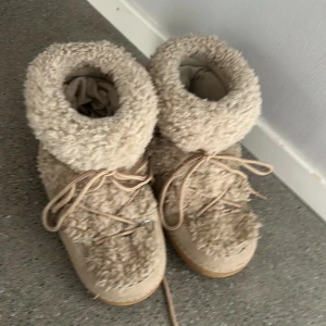 Beige fluffiga moon boots från Happy - Säljer ett par beige moon boots från Happy med fluffigt pälsmaterial och snygga snörningar framtill. 