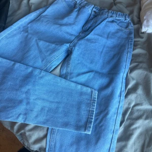 Ljusblå jeans med resårmidja - Säljer ett par ljusblå jeans med resår i midjan och raka ben. Jeansen har klassiska fickor fram och bak, och är tillverkade i mjukt denimtyg. Perfekta för en avslappnad och trendig look.