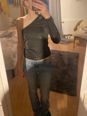 Glittrig oneshoulder topp - Säljer en svart glittrig oneshoulder topp med lång ärm på ena sidan.Endast använd 1 gång 