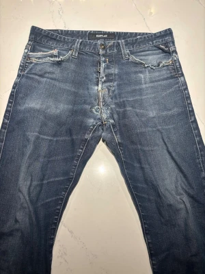Replay blå jeans, storlek 31/32 - Säljer ett par klassiska Replay jeans i blå tvätt med slitningar och snygga detaljer på fickorna. Jeansen har normal passform och raka ben, tillverkade i tåligt denimtyg. Märkespatch bak i midjan och Replay-logga på fickan framtill. Värt att notera att de är ihop sydda då de spruckit därav priset! Mvh Linus