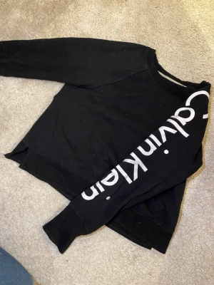 Svart tröja från Calvin Klein - Jättesnygg svart tröja från Clavin Klein med vitt tryck på ena armen. Superenkel att styla med ett par jeans eller kjol och funkar i all årstider. Jag säljer den nu så den inte är min stil längte😊🥰