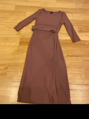 ribbad långklänning med bälte - Säljer en ribbad långklänning från bubbleroom med trekvartsärm och matchande bälte i midjan. Klänningen har en liten slits framtill för extra vibe och är i mjukt stretchigt material. Perfekt för dig som gillar stilrena och bekväma plagg.