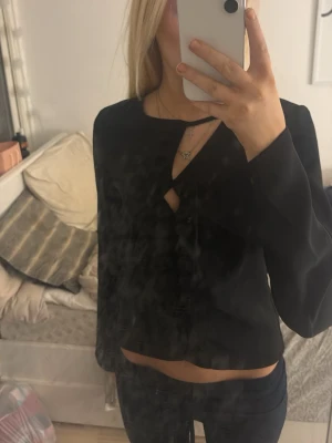 Svart croppad topp från BikBok - Säljer en svart croppad topp från BikBok i storlek XS. Toppen har lång ärm och en unik cut-out detalj vid halsen som ger en fin twist. Materialet känns mjukt och lätt, perfekt att styla med låga jeans. Använd fåtal gånger
