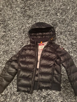 Svart dunjacka Parajumpers  - Säljer en svart Parajumpers Sheen dunjacka med huva och dragkedja. Jackan har quiltad design, ribbade muddar och ikonisk PJS-patch på ärmen. Insidan är ljusgrå och materialet är syntet med dunfyllning. Perfekt för kalla dagar och riktigt snygg streetstil. Storleken i herr är XS!!! Priset kan diskuteras 