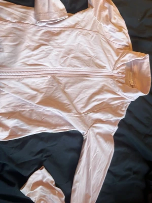 Ljusrosa ziptröja från Gina Tricot - Superskön ljusrosa ziptröja från Gina Tricot med lång ärm och tumhål. Tröjan har hög krage och dragkedja framtill, perfekt för träning eller chill. Materialet är mjukt och stretchigt syntet som sitter snyggt på kroppen.