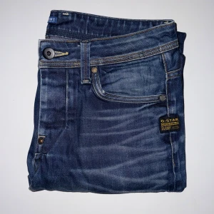 G-Star RAW Blå Jeans - Ett par blå jeans från G-Star RAW med snygga slitningar och kontrastsömmar. Materialet är robust denim och passformen är normal. De har inga stora spår av användningar och inga skador.