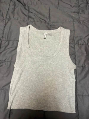 Grå ribbad linnetopp H&M Divided - Säljer en enkel och stilren grå ribbad linnetopp från H&M Divided. Toppen är ärmlös med rundad halsringning och croppad passform. Storlek S