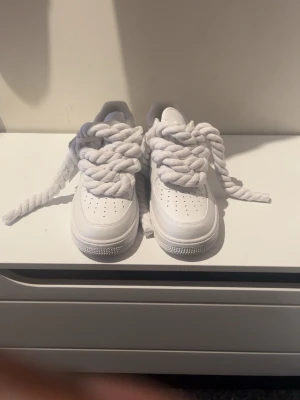 Nike Air Force 1 vita sneakers med tjocka snören - Helt nya äkta Nike Air Force 1 i limited edition sneakers i helvitt skinn med extra tjocka snören, man kan även ta bort tjocka snören om man tycker att det är för mycket. Klassisk låg modell med perforerad tå och rund sula. Swoosh-logga på sidan och AIR-detalj på hälen. Perfekta för dig som vill sticka ut med din sneakerstil.